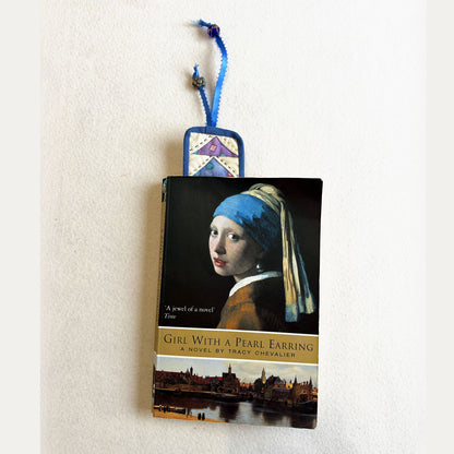 The blue Flying Geese Bookmark tucked into a paperback, with its ribbon and beads showing at the top