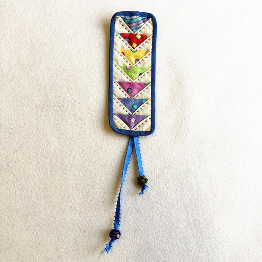 Flying Geese Bookmark: a quilted bookmark with rainbow flying geese, blue binding and a beaded ribbon tail