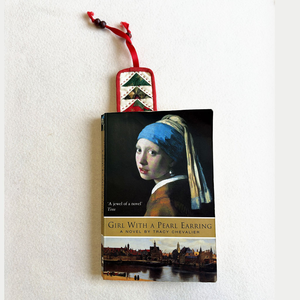The Christmas Flying Geese Bookmark tucked into a paperback, with its red ribbon and wooden beads at the top