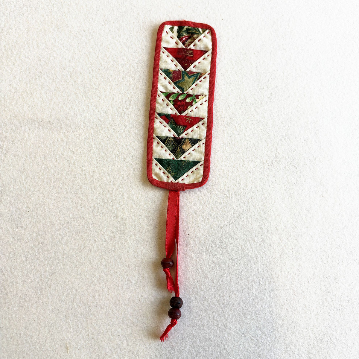 Flying Geese Bookmark in Christmas colours: red and green geese with red binding and a beaded ribbon tail