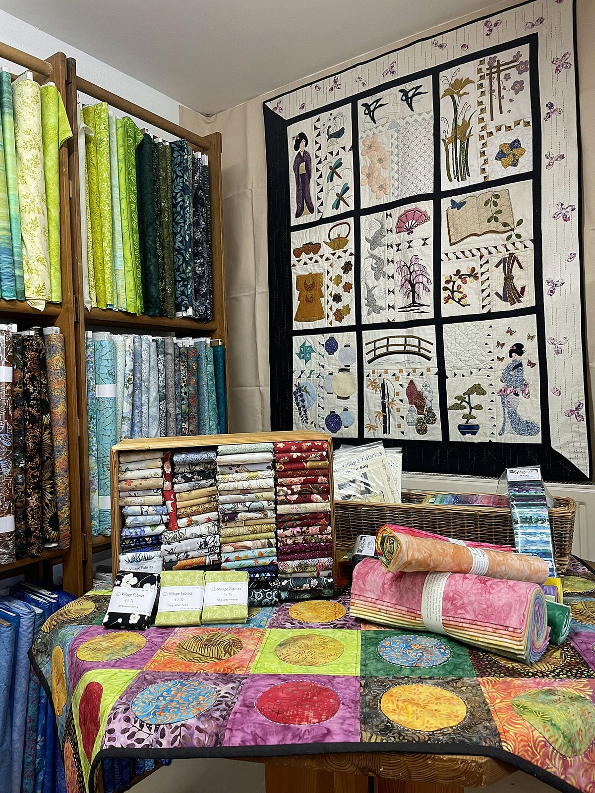 The Impressions of Japan quilt on display in the shop, above a table of Japanese fabrics and batik rolls