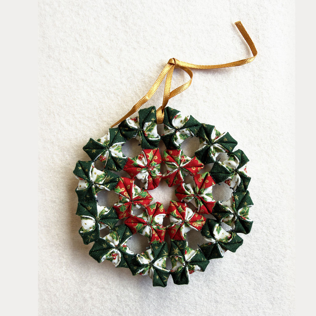 Mini Christmas Wreath made from the kit: a small folded fabric wreath in green, red and cream Christmas prints with a gold hanging ribbon