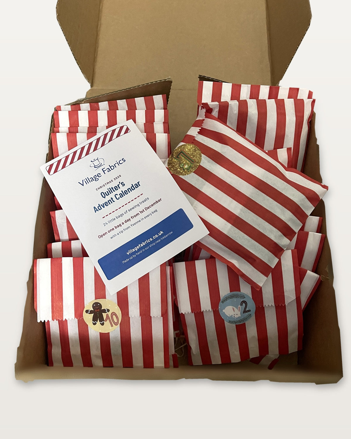 The Quilter's Advent Calendar open: 24 numbered red and white striped bags and the welcome card in the box
